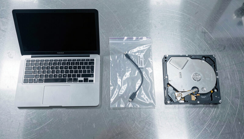 A laptop, a sealed evidence bag and a labelled hard drive arranged on a clean examination bench.